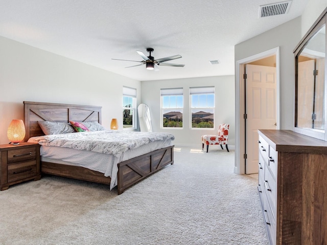bedroom featuring light carpet, a textured ceiling, visible vents, and a ceiling fan
