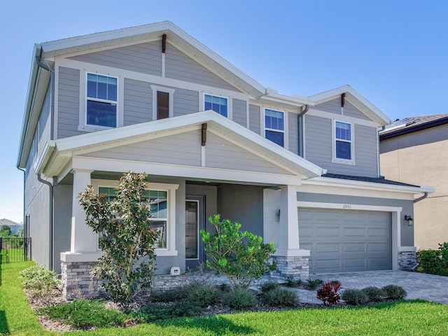 craftsman-style house featuring an attached garage, stone siding, decorative driveway, and stucco siding