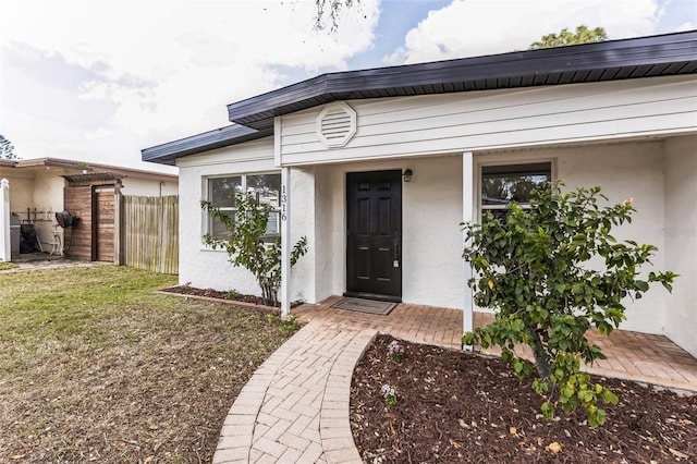 entrance to property featuring fence, a lawn, and stucco siding