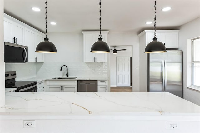 kitchen featuring stainless steel appliances, a sink, white cabinetry, decorative backsplash, and pendant lighting