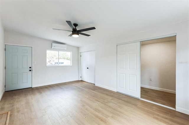 unfurnished bedroom featuring light wood-style floors, an AC wall unit, baseboards, and multiple closets