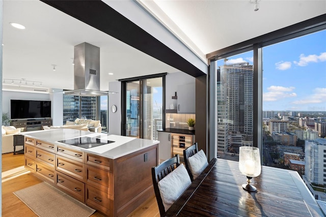 kitchen with a view of city, light wood-style flooring, black electric cooktop, island range hood, and expansive windows