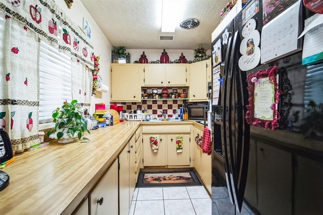 kitchen with a textured ceiling, black refrigerator with ice dispenser, light tile patterned flooring, and visible vents