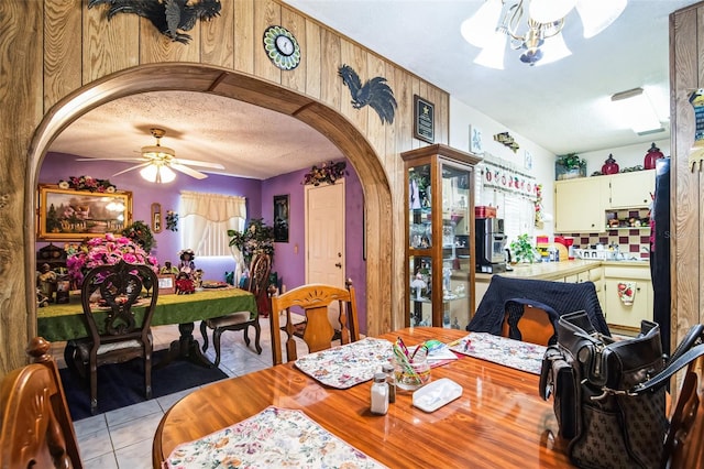 dining area featuring ceiling fan with notable chandelier, arched walkways, a textured ceiling, and light tile patterned flooring