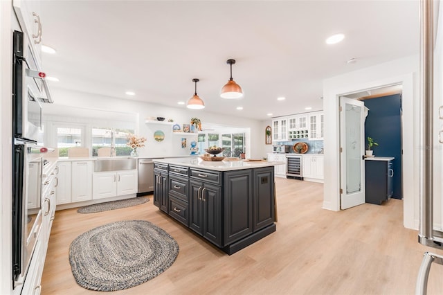 kitchen featuring light wood finished floors, beverage cooler, light countertops, white cabinetry, and stainless steel dishwasher