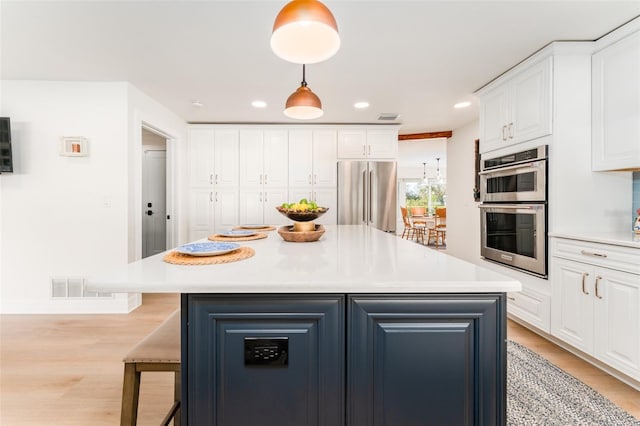 kitchen featuring light wood-type flooring, stainless steel appliances, a center island, and white cabinetry