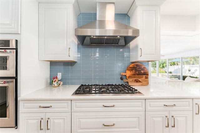 kitchen with white cabinetry, wall chimney exhaust hood, tasteful backsplash, and appliances with stainless steel finishes