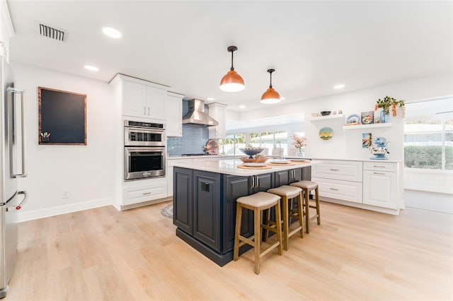 kitchen featuring light wood finished floors, white cabinetry, stainless steel appliances, and wall chimney exhaust hood