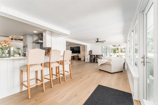 living area with light wood-style floors, a healthy amount of sunlight, a ceiling fan, and a decorative wall