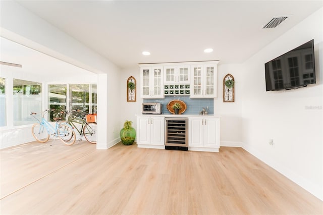 bar featuring visible vents, beverage cooler, light wood-style floors, a bar, and decorative backsplash