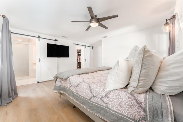 bedroom with light wood-style flooring, a ceiling fan, a walk in closet, and a barn door