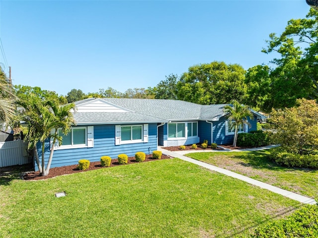 ranch-style home with a shingled roof, a front lawn, and fence