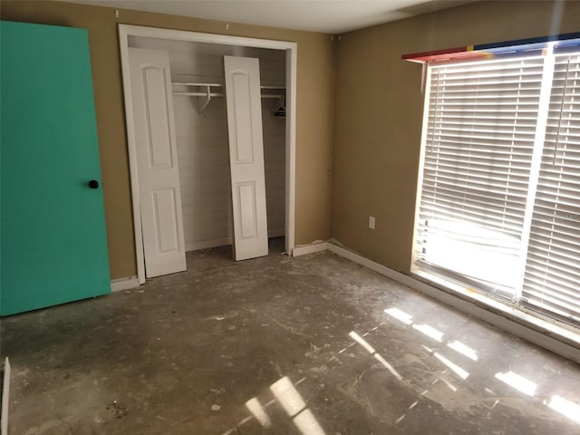 unfurnished bedroom featuring concrete flooring, a closet, and baseboards