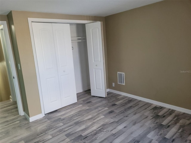 unfurnished bedroom with baseboards, visible vents, a closet, and wood finished floors