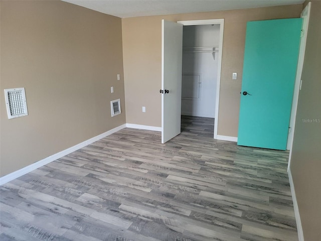 unfurnished bedroom with baseboards, visible vents, wood finished floors, a walk in closet, and a closet