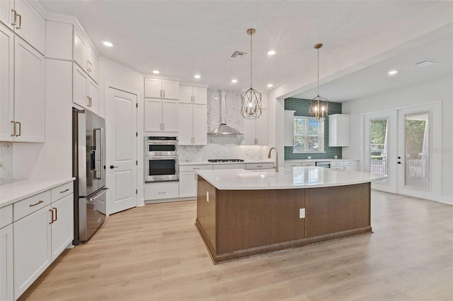 kitchen with appliances with stainless steel finishes, light wood-style floors, wall chimney range hood, and decorative backsplash