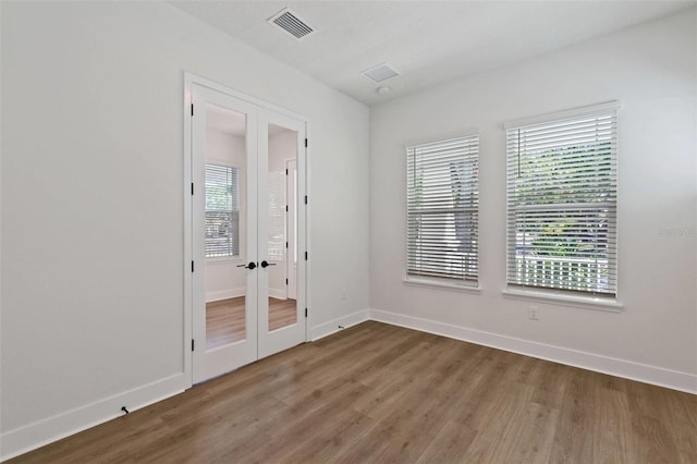 unfurnished room featuring french doors, visible vents, baseboards, and wood finished floors