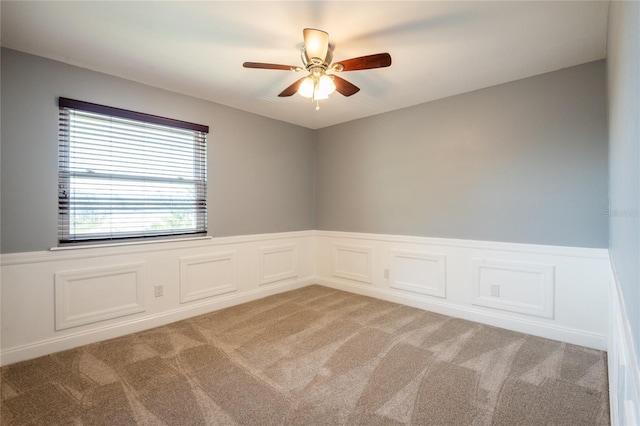 spare room featuring ceiling fan, wainscoting, and light carpet