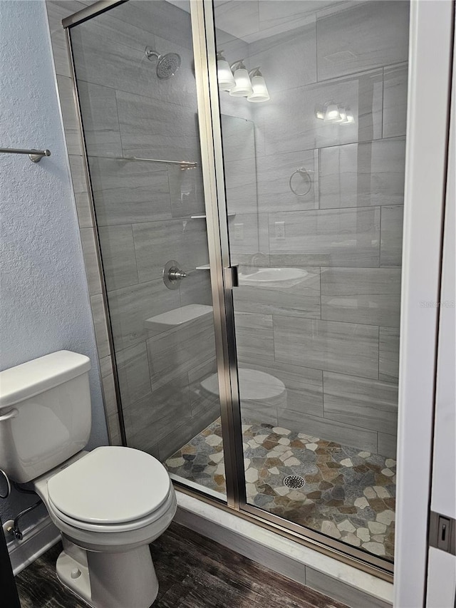 bathroom with toilet, a stall shower, wood finished floors, and a textured wall