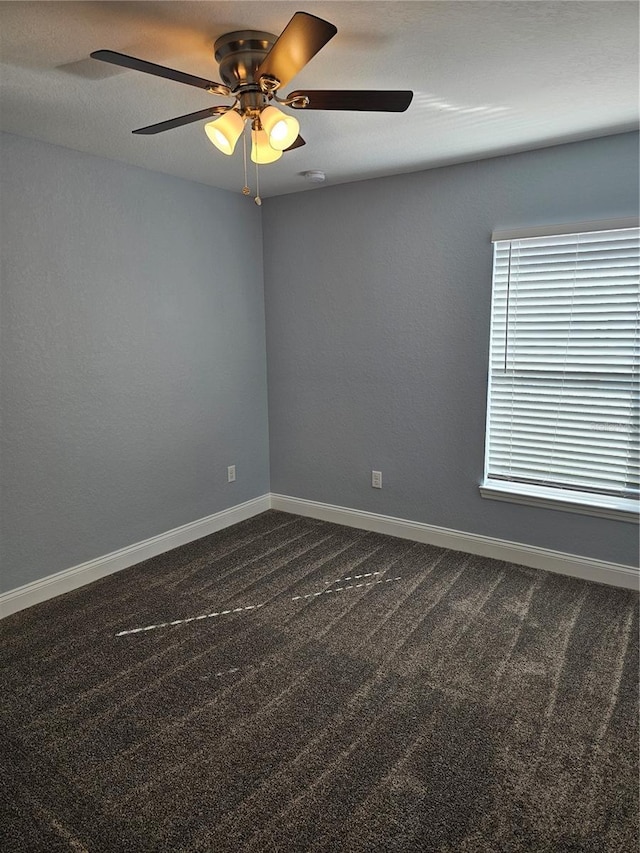 spare room with dark colored carpet, ceiling fan, and baseboards