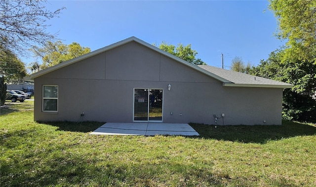 rear view of house with roof with shingles, stucco siding, a yard, and a patio