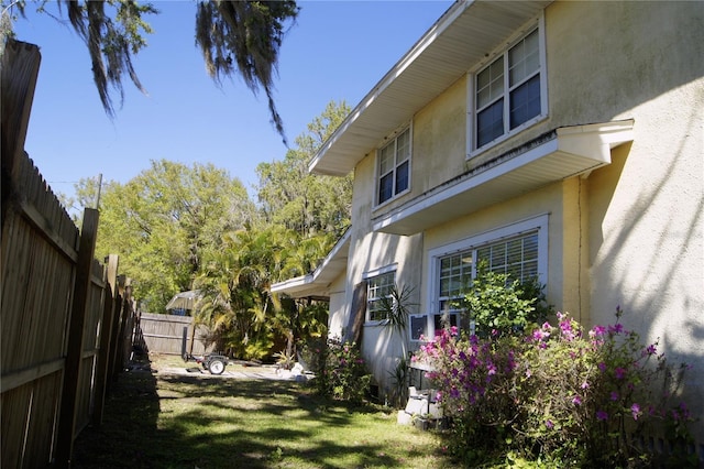 view of side of home with a lawn, fence, and stucco siding