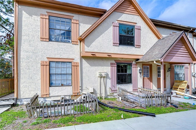 view of front facade featuring stucco siding, a shingled roof, and fence