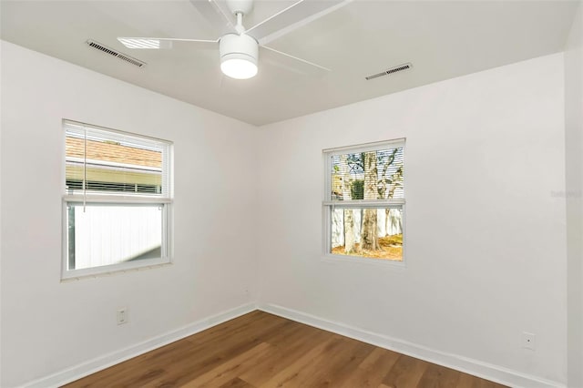 empty room featuring a ceiling fan, wood finished floors, visible vents, and baseboards