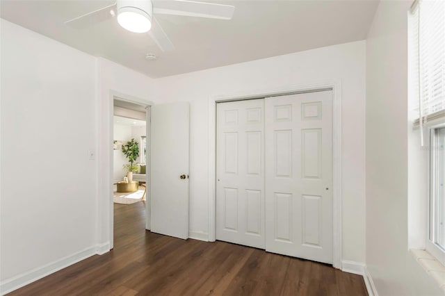 unfurnished bedroom featuring ceiling fan, a closet, baseboards, and dark wood-type flooring