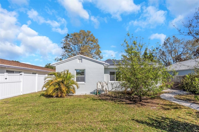 view of front facade featuring concrete block siding, fence, a front lawn, and solar panels