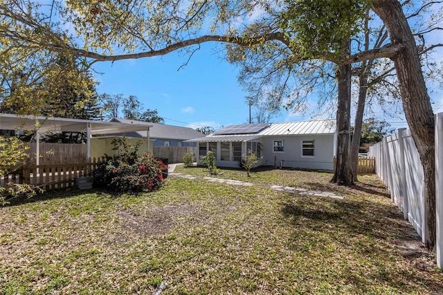 back of house featuring metal roof, a lawn, a fenced backyard, and roof mounted solar panels