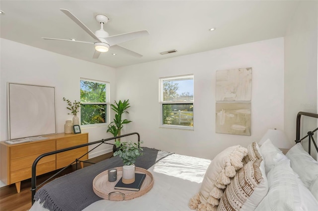 bedroom featuring a ceiling fan, multiple windows, visible vents, and wood finished floors