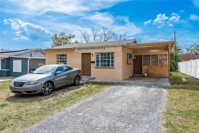 ranch-style home featuring an attached carport, a front lawn, gravel driveway, and fence