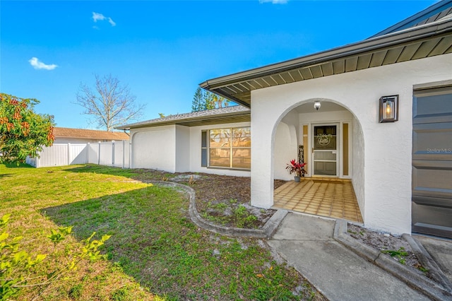 entrance to property with fence, a lawn, and stucco siding