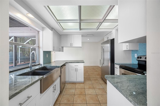 kitchen featuring light tile patterned floors, stainless steel appliances, a sink, white cabinets, and dark stone countertops