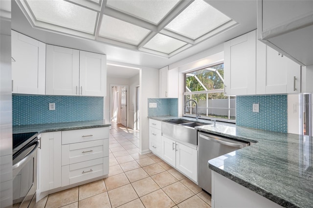 kitchen featuring appliances with stainless steel finishes, light tile patterned flooring, a sink, white cabinetry, and dark stone countertops