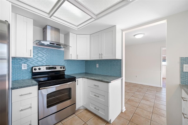 kitchen with light tile patterned floors, stainless steel appliances, white cabinets, wall chimney exhaust hood, and tasteful backsplash