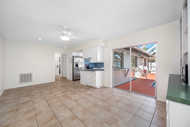 kitchen featuring stainless steel refrigerator with ice dispenser, dark countertops, visible vents, a ceiling fan, and white cabinets