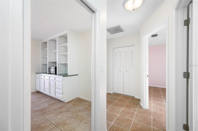 hall featuring light tile patterned floors, visible vents, and baseboards