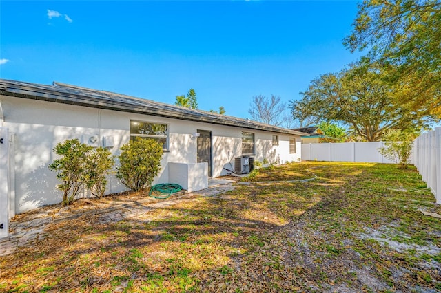 rear view of property with central air condition unit, a fenced backyard, a yard, and stucco siding