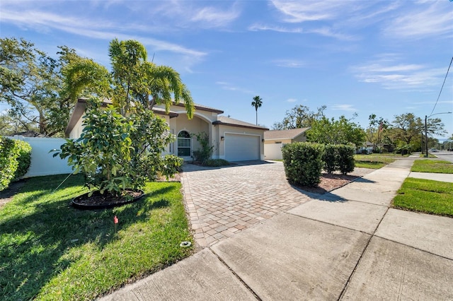 view of front of property featuring decorative driveway, stucco siding, fence, a garage, and a front lawn