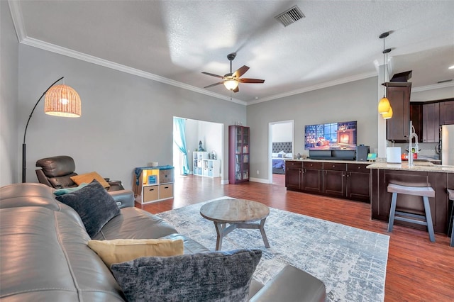 living room featuring visible vents, ceiling fan, ornamental molding, wood finished floors, and a textured ceiling