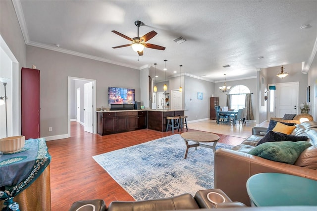 living area with ceiling fan with notable chandelier, visible vents, wood finished floors, and ornamental molding