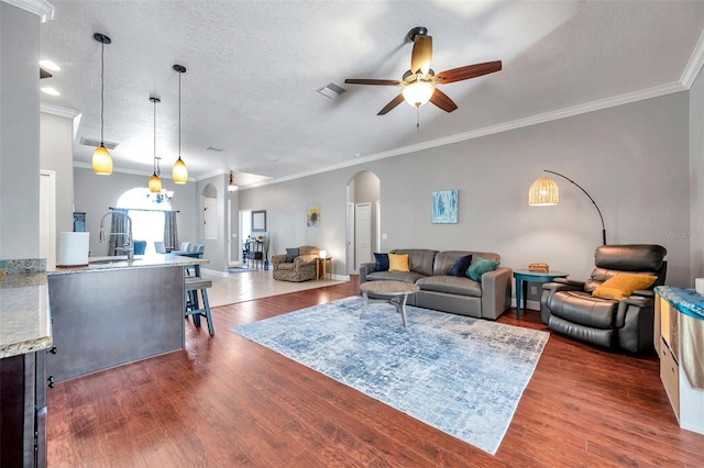 living area featuring arched walkways, a textured ceiling, dark wood-style flooring, visible vents, and a ceiling fan