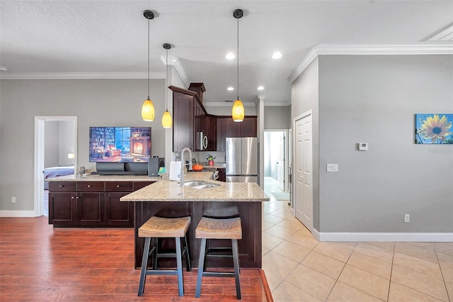 kitchen featuring freestanding refrigerator, a peninsula, light stone countertops, dark brown cabinets, and a sink