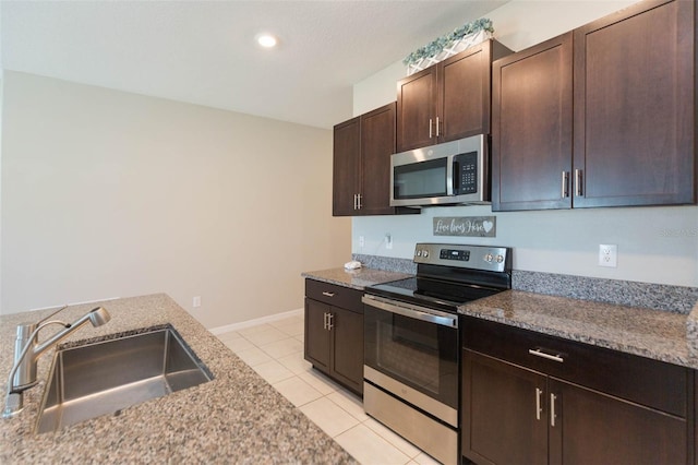 kitchen featuring light tile patterned floors, a sink, dark brown cabinets, appliances with stainless steel finishes, and light stone countertops