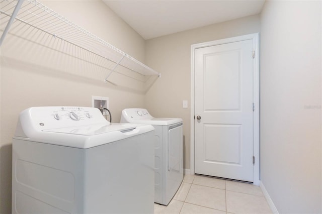 clothes washing area featuring laundry area, separate washer and dryer, light tile patterned flooring, and baseboards