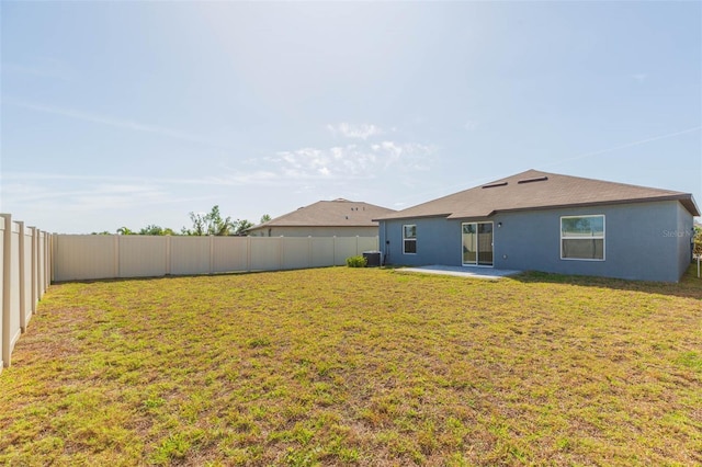 rear view of house with stucco siding, a fenced backyard, and a yard