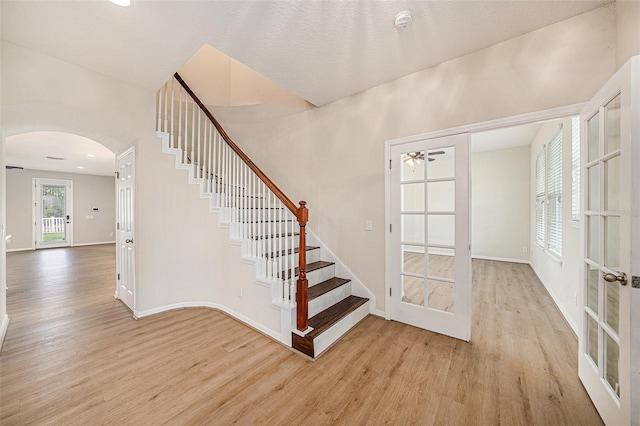 staircase with baseboards, arched walkways, and wood finished floors