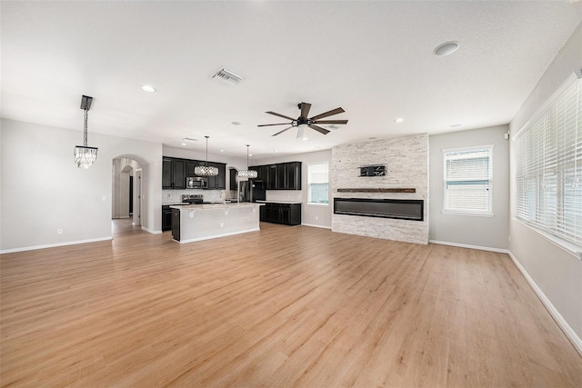 unfurnished living room with ceiling fan with notable chandelier, a fireplace, visible vents, and light wood-style floors